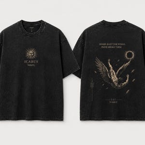 Może przedstawiać: Czarny t-shirt z efektem sprania, z grafiką słońca i napisem ICARUS z przodu. Z tyłu znajduje się postać ze skrzydłami w locie w dół, ciemne słońce oraz tekst DESIRE BUILT THE WINGS, PRIDE BROKE THEM, a na dole słowo ICARUS.