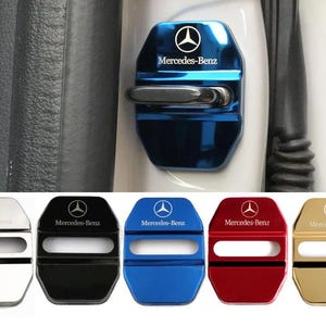 Puede incluir: Un juego de cinco cubiertas metálicas para cerraduras de puertas de coche en plata, negro, azul, rojo y oro. Cada cubierta presenta el logotipo y el texto de Mercedes-Benz grabados. Las cubiertas tienen forma rectangular con una ranura.