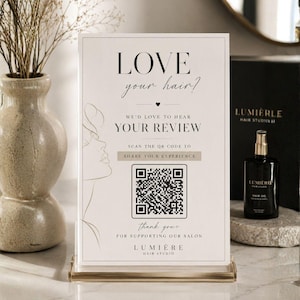 Könnte beinhalten: Ein rechteckiges weißes Schild in einem klaren Acrylständer mit schwarzem Text, der LOVE your hair? WE'D LOVE TO HEAR YOUR REVIEW, SCAN THE QR CODE TO SHARE YOUR EXPERIENCE, thank you FOR SUPPORTING OUR SALON und LUMIÈRE HAIR STUDIO lautet.