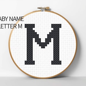 May include: Cross-stitch embroidery hoop featuring the letter "M" in black on a white background. The text "BABY NAME LETTER M" is above the letter. The hoop is round with a wooden frame.