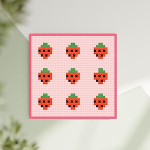 May include: A cross-stitch design featuring nine pixelated strawberries. Each strawberry is red with a green top and black seeds, set against a light pink background with a pink border. The design is square and appears to be a finished piece of needlework.