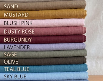May include: A pile of folded fabric swatches in a range of colours. The colours include white, ivory, oatmeal, sand, mustard, blush pink, dusty rose, burgundy, lavender, sage, olive, teal blue, sky blue, dusty blue, navy, and black. Each swatch is labelled.