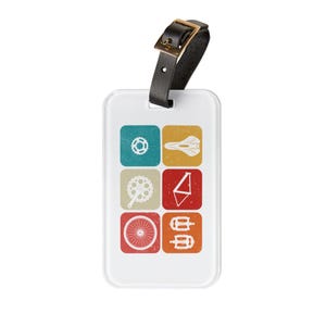 May include: A white luggage tag with a black leather strap and gold buckle. The tag features six colorful squares with bicycle-related icons: a gear, a bike seat, a chainring, a bike frame, a wheel, and pedals.