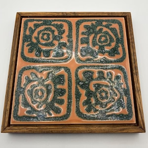 Peut inclure: Carreau de céramique carré avec un cadre en bois. Le carreau a un fond pêche avec quatre motifs floraux stylisés vert foncé. Le cadre en bois est de couleur marron moyen.