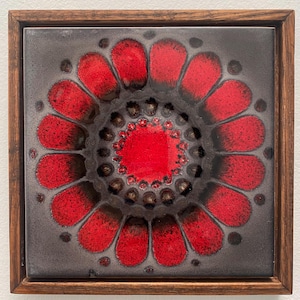 May include: Square ceramic tile with a floral design in a wooden frame. The flower has red petals and a red center, set against a gray background. The frame is a warm brown color.