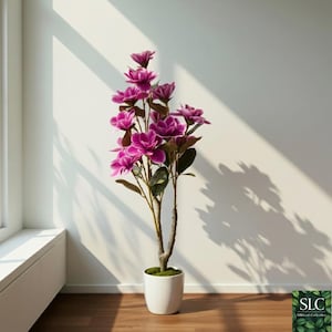 Puede incluir: Una planta floreciente artificial con vibrantes flores magenta y hojas verdes. La planta está en una maceta de cerámica blanca, contra una pared blanca con sombras. La planta mide aproximadamente 120 cm de altura.