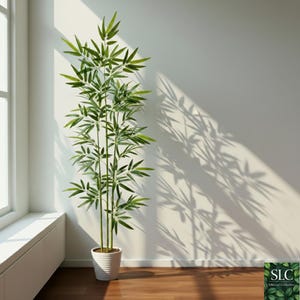 Puede incluir: Una planta de bambú artificial alta en una maceta blanca. La planta tiene múltiples tallos con hojas verdes. La maceta es cilíndrica con estrías horizontales. La planta está frente a una pared blanca, con sombras de bambú.