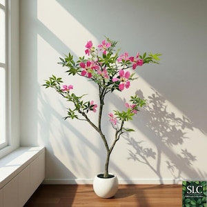 Puede incluir: Un árbol artificial en maceta con flores rosas y hojas verdes. El árbol está en una maceta blanca y se encuentra contra una pared blanca. La sombra del árbol se proyecta en la pared. Es un objeto decorativo.