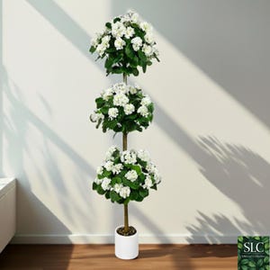 Puede incluir: Una planta topiaria artificial de tres niveles con flores blancas y hojas verdes. La planta está en una maceta blanca y tiene un tallo marrón. La planta está contra una pared blanca con sombras.