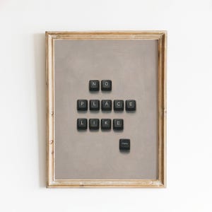 May include: A framed wall art piece featuring a light gray background with black computer keyboard keys arranged to spell out the phrase NO PLACE LIKE HOME. The keys are positioned in three rows with the word Home placed separately below.