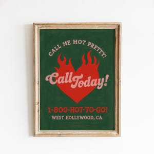 May include: Framed poster with a dark green background and a red heart-shaped flame design. The text "CALL ME HOT PRETTY!" arcs above the flame, with "Call Today!" in a cursive font. The bottom text reads "1-800-HOT-TO-GO! WEST HOLLYWOOD, CA".