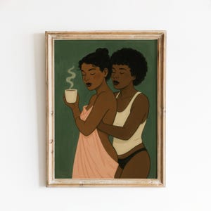 May include: Art print featuring two women embracing. One holds a cup of coffee with steam rising, wrapped in a pink towel. The other wears a white tank top and black underwear. The background is a muted green, framed in a light wood.