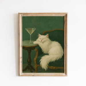 May include: A framed print showing a white cat relaxing on a green armchair beside a small table with a martini. The cat rests its paw on the table, with a martini glass containing olives. The background is a dark green.