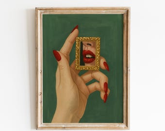 May include: A framed art print featuring a hand with long red nails holding a small gold frame. The frame displays a close-up of red lips against a green background. The artwork is in a wooden frame.