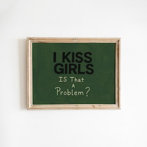 May include: A framed chalkboard with the text "I KISS GIRLS IS THAT A PROBLEM?" in black and white. The chalkboard has a dark green background and a light brown wooden frame. The text is centered on the board.