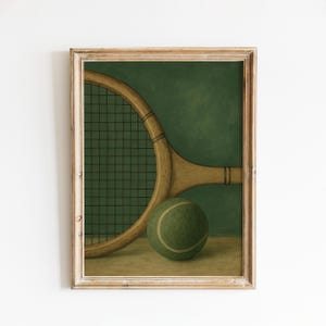 May include: A framed print featuring a vintage tennis racket and ball. The racket is light brown with a dark mesh, and the tennis ball is green with a white stripe. The background is a dark green.