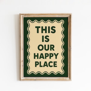 May include: Framed wall art with the text "THIS IS OUR HAPPY PLACE" in dark green lettering. The text is centered on a cream-colored background with a dark green scalloped border, all within a light brown wooden frame.