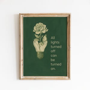 Può includere: Stampa artistica incorniciata con sfondo verde e design a lampadina. All'interno della lampadina c'è un fiore e una farfalla. Il testo recita "All lights turned off can be turned on."