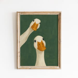 May include: Framed art print featuring two white geese with orange beaks and dark eyes against a deep green background. The geese are positioned in a whimsical, slightly askew manner, creating a playful and engaging composition.