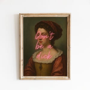 May include: Framed art print featuring a portrait of a woman in a red and gold dress and a red head covering. The words "Don't be a dick" are written in pink neon-style script across the image.