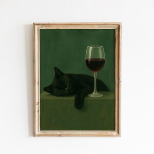 Op de afbeelding: Een ingelijste prent met een zwarte kat die naast een wijnglas met rode wijn slaapt. De kat rust op een groen oppervlak tegen een donkergroene achtergrond. Het kunstwerk heeft een vintage esthetiek.