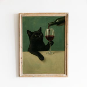 May include: A framed print shows a black cat holding a wine glass, with red wine being poured into it from a bottle. The cat has a serious expression. The background is a muted green.