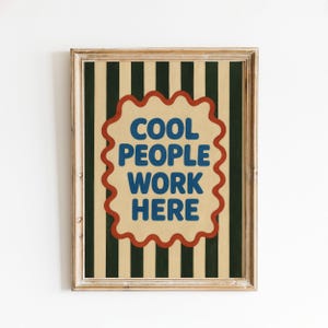 May include: A framed wall art print featuring vertical dark green and beige stripes. In the center, a scalloped-edge beige shape with a red border contains the blue text COOL PEOPLE WORK HERE, written in a bold, rounded, sans-serif typeface.
