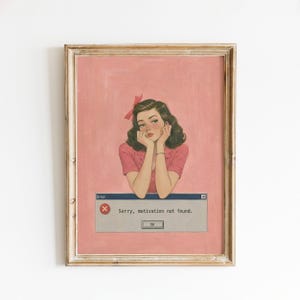 Op de afbeelding: Een ingelijste kunstdruk met een retro-stijl illustratie van een persoon met donker golvend haar en een roze strik, rustend met de kin op de handen tegen een roze achtergrond. Onderaan toont een foutmelding het tekstbericht: Sorry, motivation not found.