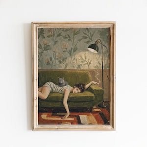 May include: A framed art print depicting a person in a striped dress lying on a green sofa with a gray cat. A black floor lamp stands beside the sofa, which is set against a wall with floral wallpaper and a patterned rug on the floor below.