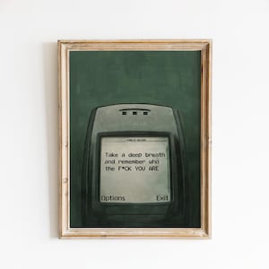Op de afbeelding: Ingelijste kunstdruk met een vintage Nokia-telefoon met de tekst "Take a deep breath and remember who the F*CK YOU ARE". Het kunstwerk heeft een groene achtergrond en een houten lijst.