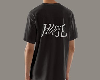 May include: Dark gray t-shirt with the word "HOUSE" printed in white on the back. The text has a stylized, flowing font. The shirt is a basic crew neck style.