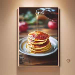 May include: A framed print of a stack of golden pancakes on a white plate, with syrup being poured over them. The image has a warm, inviting feel, with red apples in the background. The pancakes are a breakfast food.
