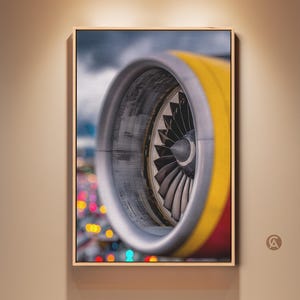 Könnte beinhalten: Nahaufnahme eines Flugzeugtriebwerks, gerahmt in einem Holzrahmen. Das Triebwerk hat einen silbernen Außenring, einen gelb-roten Körper und einen Lüfter mit mehreren Blättern. Der Hintergrund ist verschwommen mit bunten Lichtern.