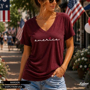 Peut inclure: Un t-shirt bordeaux &agrave; col en V avec le mot america &eacute;crit en lettres cursives blanches, surmont&eacute; d'un petit c&oelig;ur rouge au-dessus du i. Ce v&ecirc;tement &agrave; manches courtes pr&eacute;sente une coupe d&eacute;contract&eacute;e et un tissu l&eacute;ger &agrave; la texture chin&eacute;e.