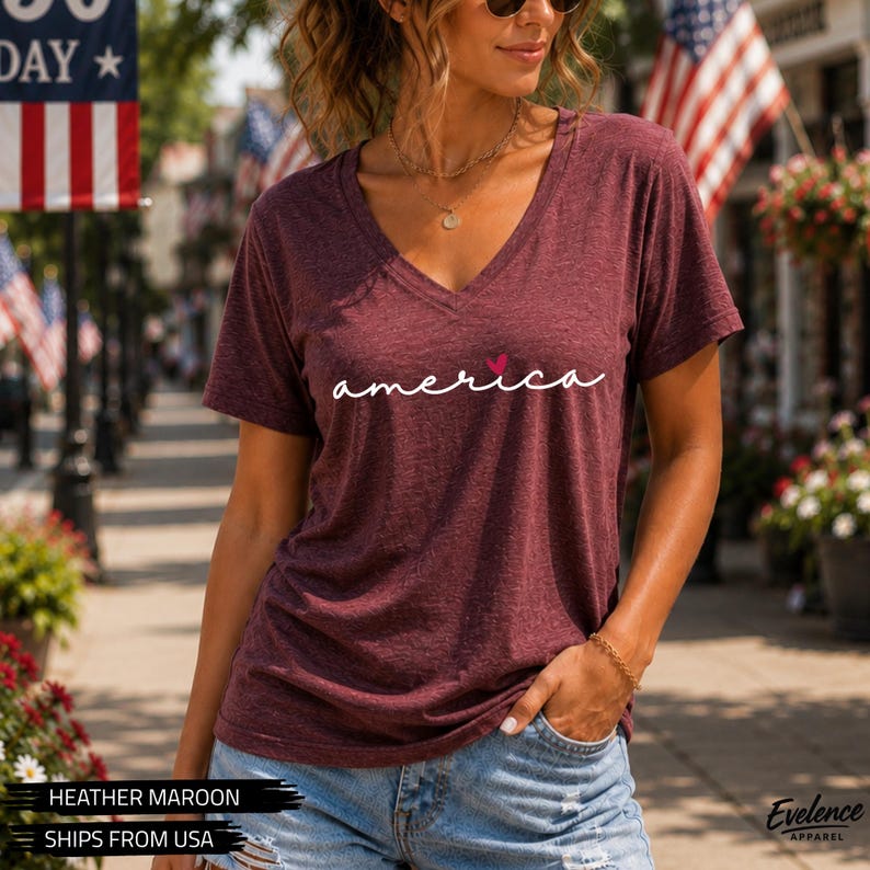 Peut inclure: Un t-shirt &agrave; manches courtes de couleur bordeaux chin&eacute; avec une encolure en V. Le devant du t-shirt pr&eacute;sente le mot "america" imprim&eacute; en &eacute;criture cursive blanche avec une petite ic&ocirc;ne de c&oelig;ur rouge plac&eacute;e au-dessus de la lettre "i".