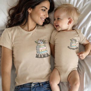 May include: Tan t-shirt and onesie set. The t-shirt has a graphic of a stack of books with flowers and the word "MAMA". The onesie has a similar graphic with the words "CHAPTER ONE".