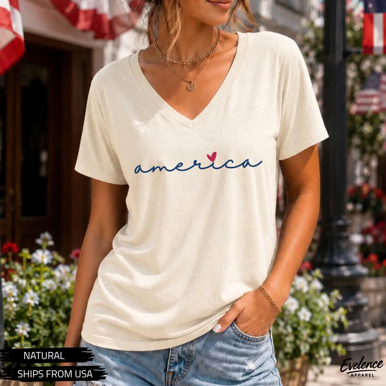 Peut inclure: Un t-shirt &agrave; manches courtes de couleur cr&egrave;me avec une encolure en V. Le devant pr&eacute;sente le mot "america" &eacute;crit en lettres cursives bleu fonc&eacute;, avec un petit c&oelig;ur rouge rempla&ccedil;ant le point sur la lettre i. Le t-shirt est port&eacute; avec un jean bleu.