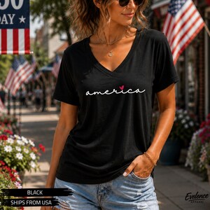 Peut inclure: Un t-shirt noir &agrave; manches courtes et col en V avec le mot america &eacute;crit en &eacute;criture cursive blanche, surmont&eacute; d'un petit c&oelig;ur rouge au-dessus de la lettre i. Le v&ecirc;tement est compos&eacute; d'un tissu l&eacute;ger et pr&eacute;sente une coupe d&eacute;contract&eacute;e.