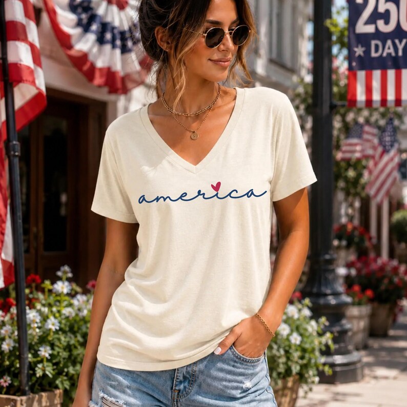 Peut inclure: Un t-shirt &agrave; manches courtes de couleur cr&egrave;me avec une encolure en V. Le devant du t-shirt pr&eacute;sente le mot "america" &eacute;crit dans une police cursive bleu fonc&eacute;, avec un petit c&oelig;ur rouge positionn&eacute; au-dessus de la lettre i du mot america.