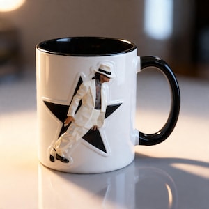 May include: White ceramic mug with a black interior and handle. The mug features a raised relief of a figure in a white suit and hat, leaning against a black star. A stylish coffee mug for any fan.