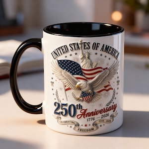 Puede incluir: Taza de cerámica blanca con asa y borde negros. La taza presenta un diseño patriótico con un águila, la bandera estadounidense y el texto "United States of America 250th Anniversary 1776-2026 Celebrating Freedom."