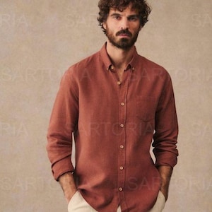 Puede incluir: Camisa de manga larga color óxido con bolsillo en el pecho. La camisa se combina con pantalones color crema. La camisa tiene un cuello clásico y botones de madera. El modelo lleva la camisa y los pantalones.