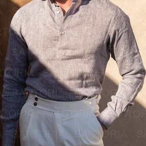 May include: A gray long-sleeve shirt with a button-down collar and white pants. The shirt has a textured appearance. The pants have a high waist and button details. The image is well-lit, showcasing the details of the clothing.