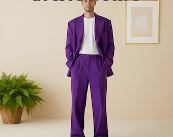 May include: A person in a striking purple suit, comprising a blazer and trousers, worn with a white t-shirt and white trainers. The word "SARTORIA" is above. The background is a neutral beige. The suit is a bold fashion statement.