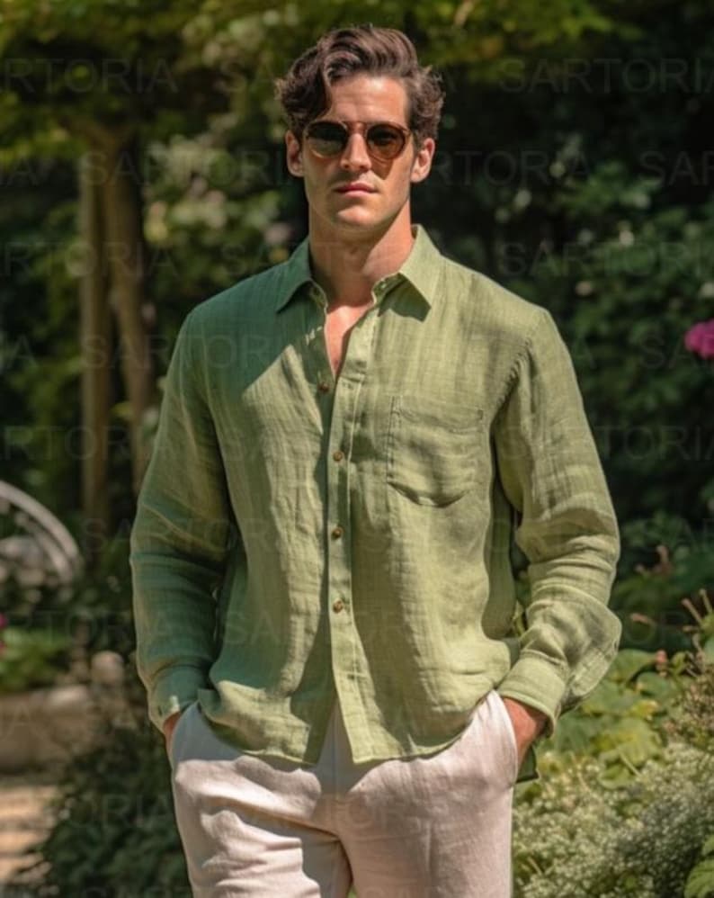 May include: A man in a light green linen shirt and beige trousers, with sunglasses. The shirt is unbuttoned at the top, and he has his hands in his pockets. The background is a blurred outdoor scene. The shirt has a chest pocket.