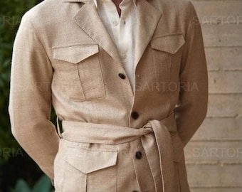Op de afbeelding: Beige safarijas met vier voorzakken, een ceintuur in de taille en knoopsluitingen. De jas wordt gecombineerd met een wit overhemd en lichtgekleurde broek. De tekst "SARTORIA" is zichtbaar.