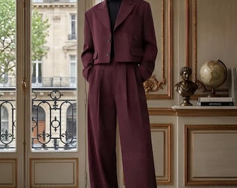 May include: A burgundy two-piece suit with a cropped blazer and wide-leg trousers. The suit is worn over a black roll neck. The outfit is a modern take on classic tailoring, suitable for formal or semi-formal occasions.