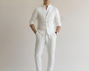 Op de afbeelding: Een wit linnen pak bestaande uit een shirt met lange mouwen, een vest en een broek. Het shirt heeft een mandarijnkraag en het vest is geknoopt. De broek is op maat gemaakt. De outfit wordt gecombineerd met bruine leren loafers en een polshorloge.