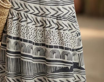 May include: A beige skirt featuring a repeating black graphic print of horizontal bands. The pattern includes rows of semicircles, chevron arrows, dotted sections, and vertical lines arranged in a stacked design across the fabric surface.