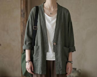 May include: An olive green linen jacket with a single button closure and two front pockets. The jacket is worn over a white top and paired with brown pants. A black shoulder bag and a watch are also visible.